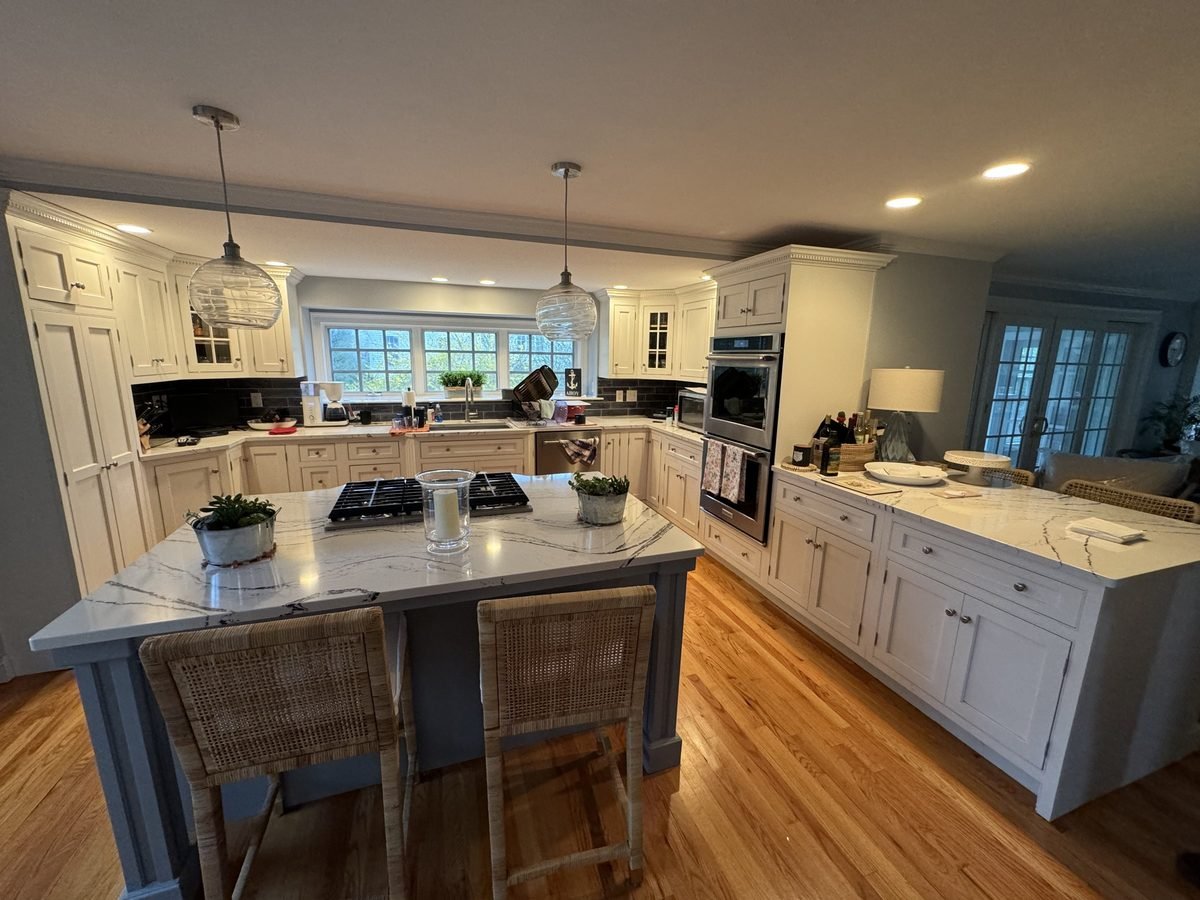 Kitchen with white cabinetry, a soft blue island and lit glass pendants