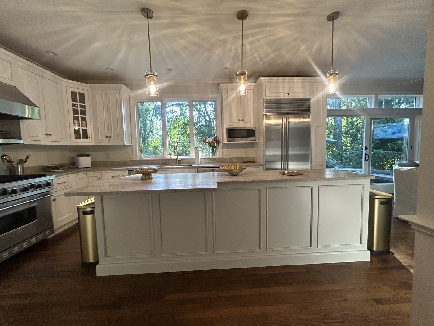 Kitchen with a painted island, glass pendants and a full wall of white cabinetry