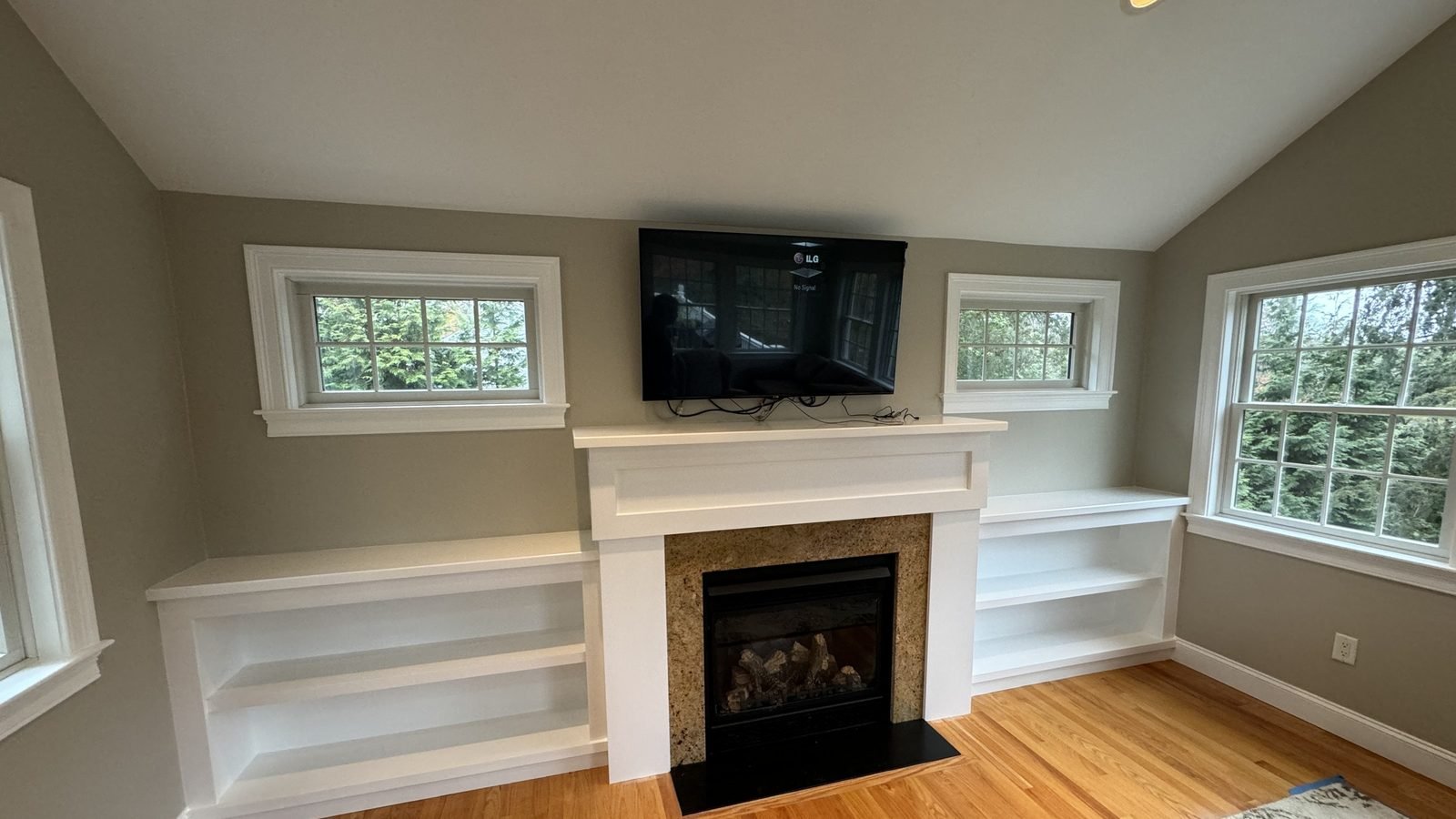 Living room with white built-in shelving, a painted fireplace mantel and a vaulted ceiling