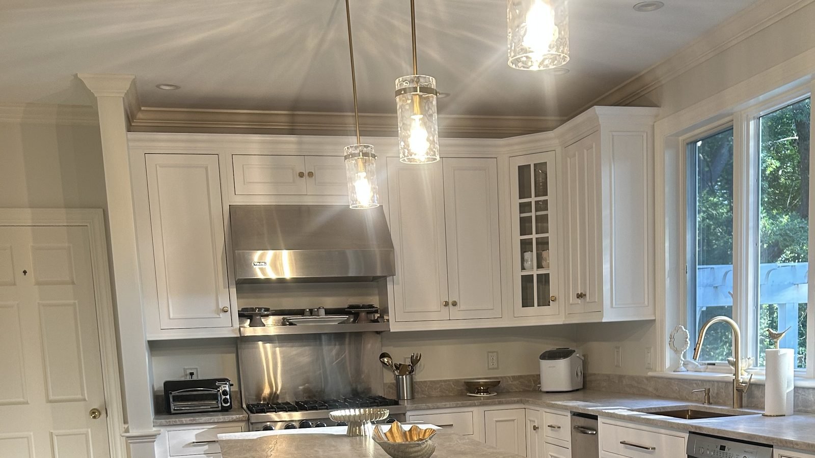 Three lit glass pendants above freshly painted white kitchen cabinetry and custom trim